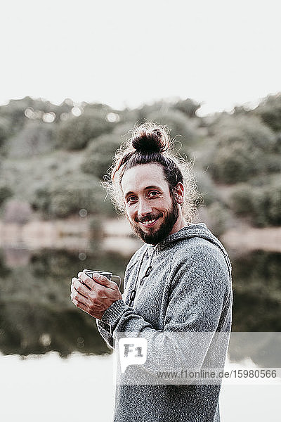 Porträt eines lächelnden Mannes mit Kaffeetasse am Seeufer
