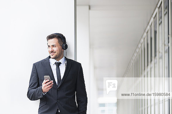 Geschäftsmann hört Musik über Kopfhörer und hält sein Smartphone im Freien