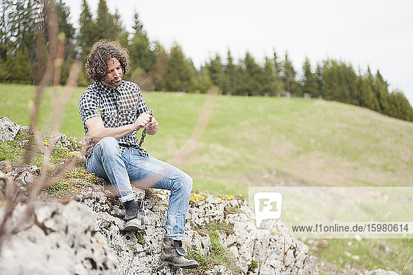Mann hält Stock  während er auf einer Felsformation sitzt