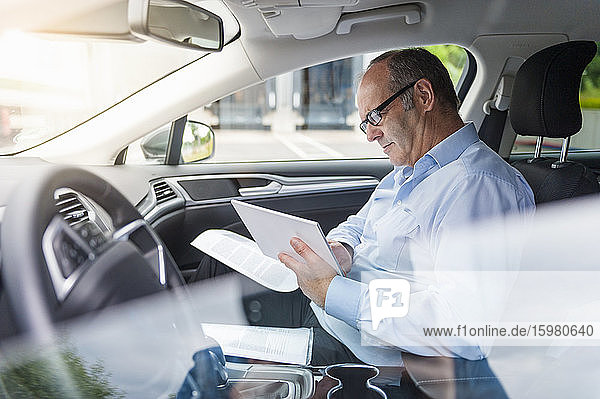 Geschäftsmann  der ein digitales Tablet benutzt  während er im Auto sitzt