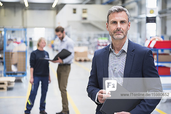 Porträt eines selbstbewussten reifen Geschäftsmannes in einer Fabrik mit Kollegen im Hintergrund