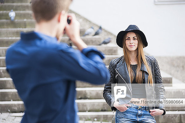 Man photographing fashionable woman through camera on steps in city