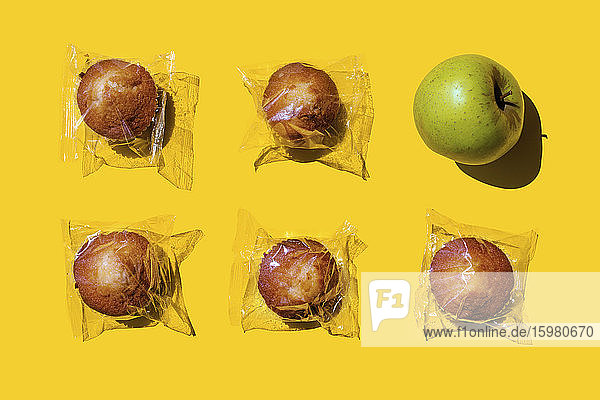 Studio shot of single apple and five plastic wrapped muffins