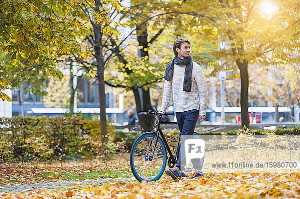 Young man pushing his bicycle in autumnal park