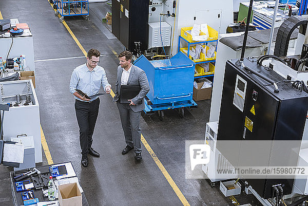 Two businessmen with clipboard talking in factory