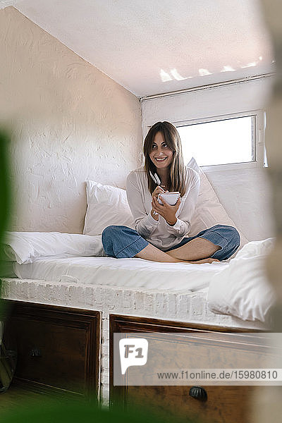 Portrait of smiling woman sitting on bed taking notes