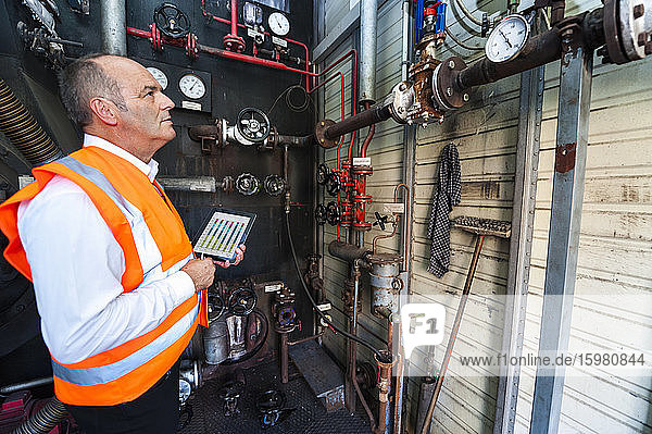 Senior man with tablet wearing safety vest examining a machine