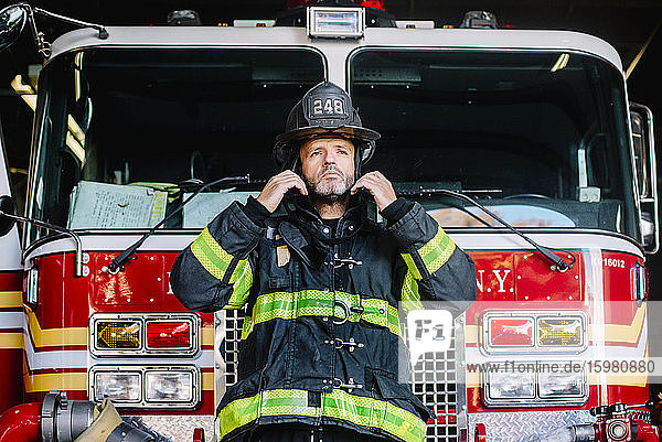 USA  New York  Porträt eines Feuerwehrmanns  der seinen Helm vor einem Feuerwehrauto aufsetzt
