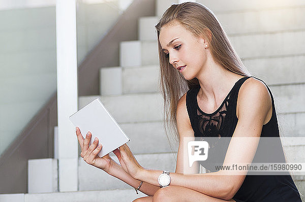 Porträt einer jungen Frau  die auf einer Treppe sitzt und ein Mini-Tablet benutzt