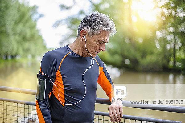 Aktiver älterer Mann  der am Geländer im Park auf seine Smartwatch schaut