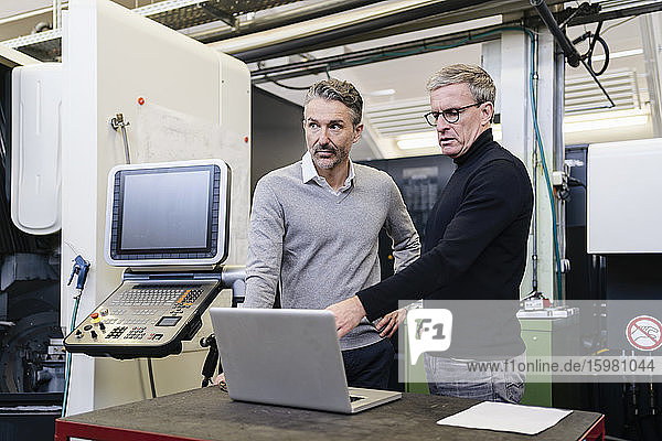 Mature male supervisors discussing over laptop in factory