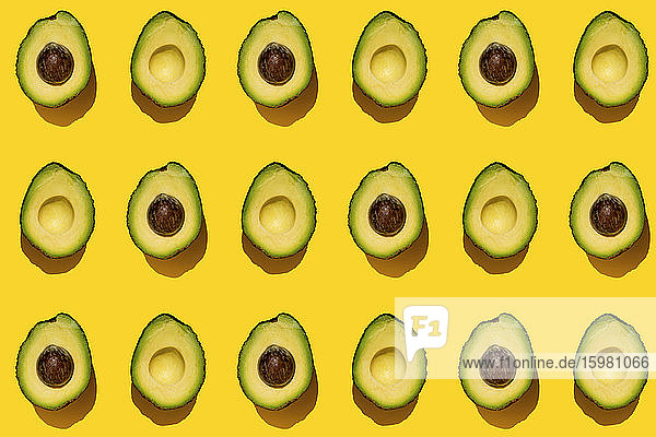 Pattern of halved avocados on yellow background