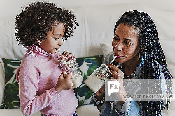 Mutter und ihre kleine Tochter trinken Smoothies zu Hause