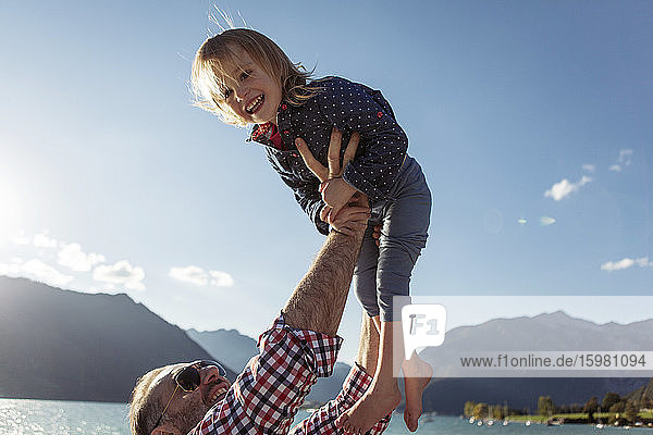 Vater hält seine fröhliche Tochter gegen den blauen Himmel am Achensee  Bundesland Tirol  Österreich  in die Höhe