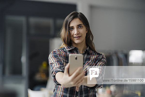Porträt einer lächelnden jungen Frau  die ein Selfie in einem Loft macht