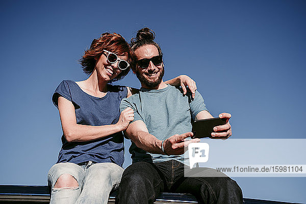 Glückliches Paar  das auf dem Dach eines Minivans sitzt und ein Selfie macht
