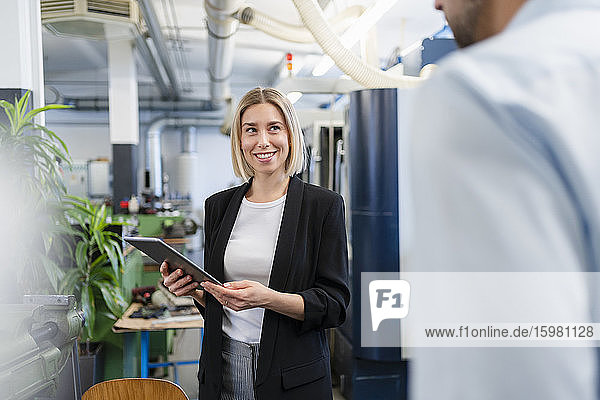 Smiling woman with tablet and businessman in factory hall