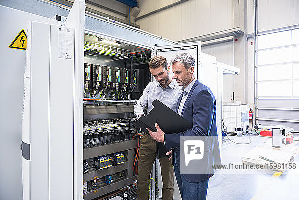 Two businessmen at a circuitry in a factory