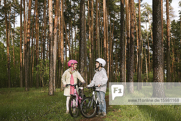 Mädchen und Junge stehen mit Fahrrädern im Wald