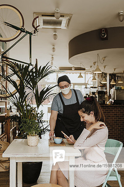 Kellnerin mit Schutzmaske serviert Cappuccino in einem Café