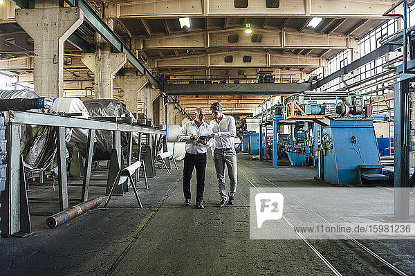 Two businessmen having a meeting looking at tablet in a factory hall