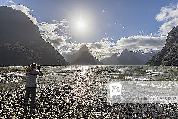 New Zealand  Female tourist photographing scenic landscape of Milford Sound