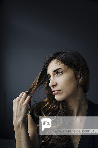 Portrait of daydreaming young woman against grey background