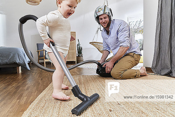 Süßes Baby Junge Reinigung Teppich mit Staubsauger von Vater im Wohnzimmer zu Hause