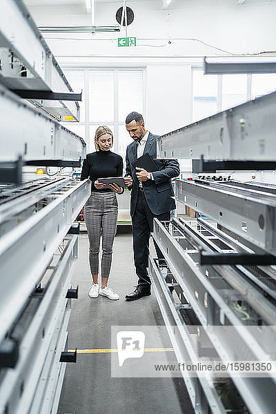 Businessman and woman with tablet at metal rods in factory hall