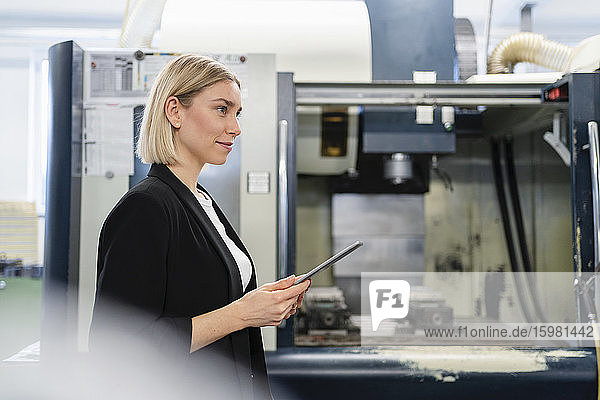 Lächelnde Frau mit Tablet in einer Fabrikhalle