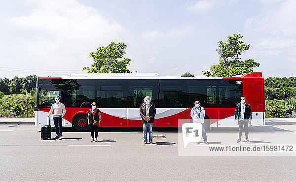 Fünf Fahrgäste mit Schutzmasken stehen in einer Reihe vor einem Linienbus  Spanien