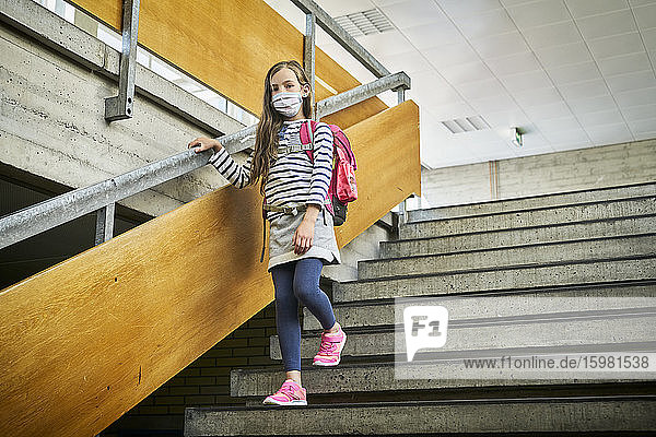 Mädchen mit Maske in der Schule geht die Treppe hinunter