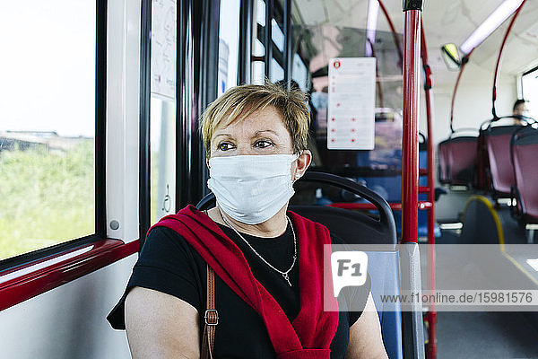 Porträt einer reifen Frau mit Schutzmaske in einem öffentlichen Bus  die aus dem Fenster schaut  Spanien