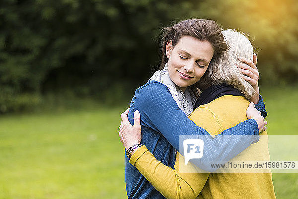 Porträt einer glücklichen Frau mit geschlossenen Augen  die ihre Mutter in einem Park umarmt