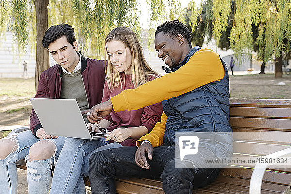 Freunde sitzen auf einer Parkbank und teilen sich einen Laptop
