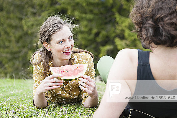 Smiling woman holding watermelon while lying by man on grass