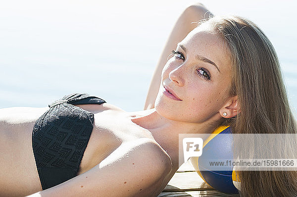 Porträt einer lächelnden jungen Frau  die sich auf einem Steg am See entspannt