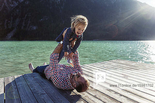Vater hält seine fröhliche Tochter im Arm  während sie auf der Uferpromenade am Achensee liegt  Bundesland Tirol  Österreich