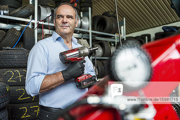 Confident senior businessman holding impact wrench while looking away at tire store