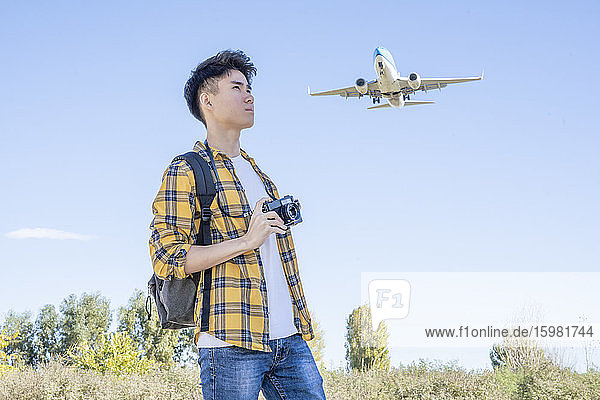 Junger Tourist mit Kamera in der Natur mit Flugzeug über ihm