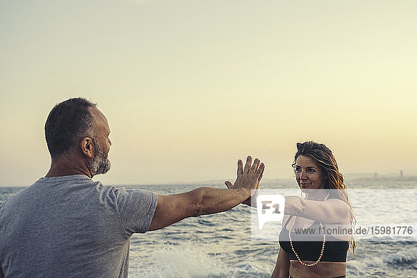 Mature couple touching hands at beach during sunset