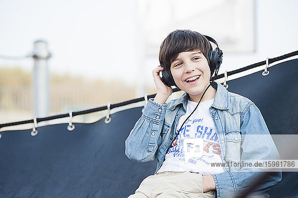 Cheerful boy looking away while listening music on hammock at park