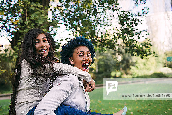 Cheerful mother piggybacking daughter while standing in park