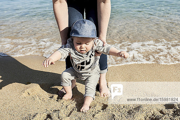 Tiefschnitt einer Mutter  die ihrem Sohn beim Gehen am Sandstrand hilft