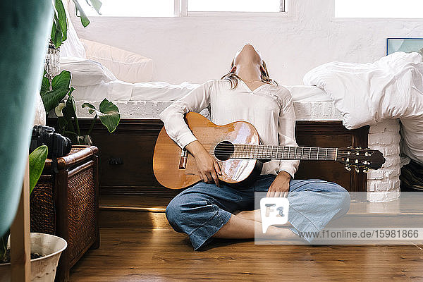 Woman with guitar sitting on the floor in front of bed leaning back