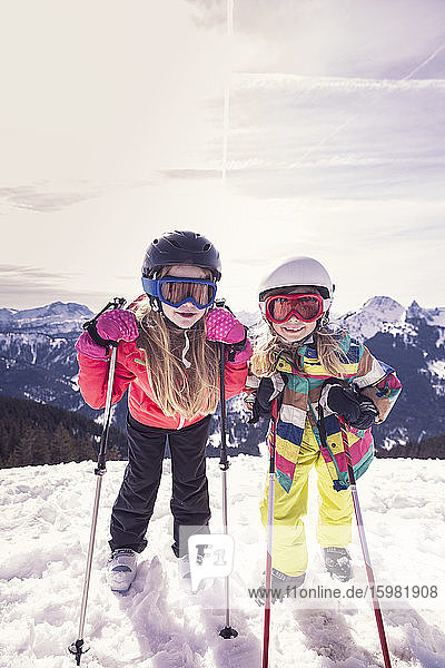 Aufgeregte Schwestern mit Skiern auf einem verschneiten Berg im Winter am Spitzingsee  Bayern  Deutschland