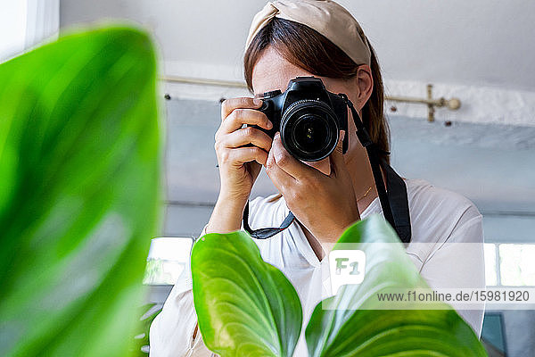 Woman photographing plant in bedroom at home