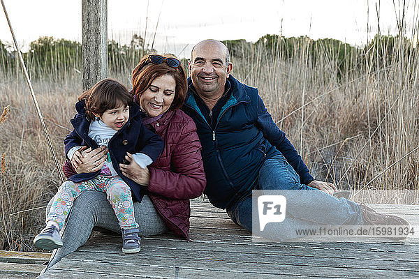 Smiling grandparents with granddaughter sitting on floorboard at countryside