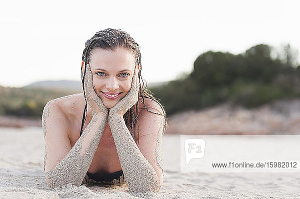 Portrait of smiling woman lying on the beach with head in her hands  Sardinia  Italy