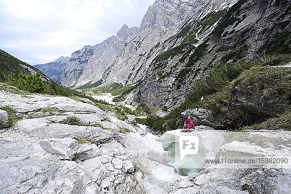 Ältere Frau erkundet die Berge  während sie am Bach sitzt